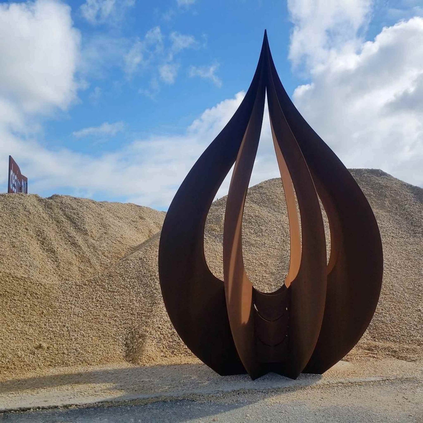 Three dimensional raindrop sculpture made from mild steel with a coastal stone backdrop