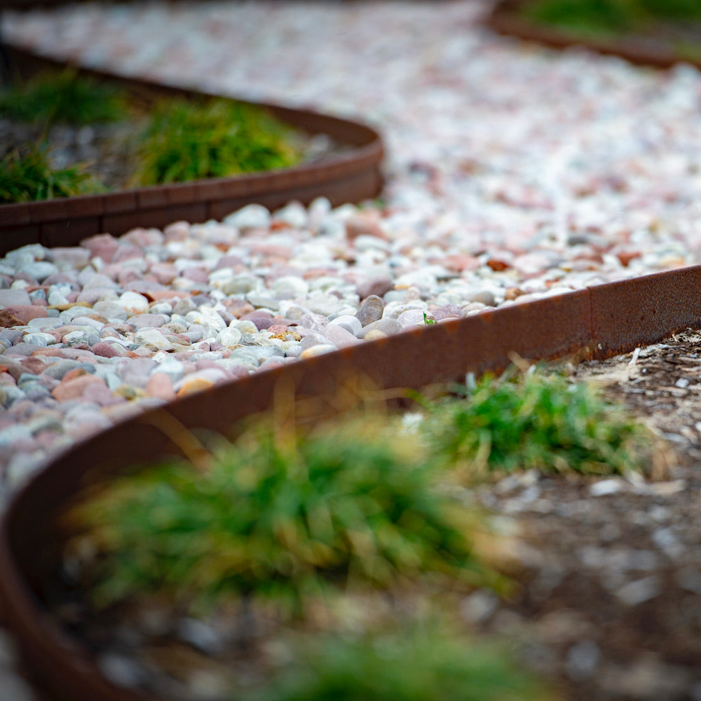 flexible corten garden edging with a rust finsih used to retain a curved river stone path